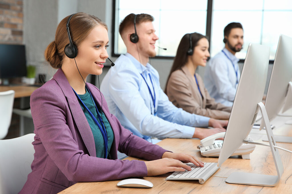 Telecom customer support team working at computers with headsets in a modern office.