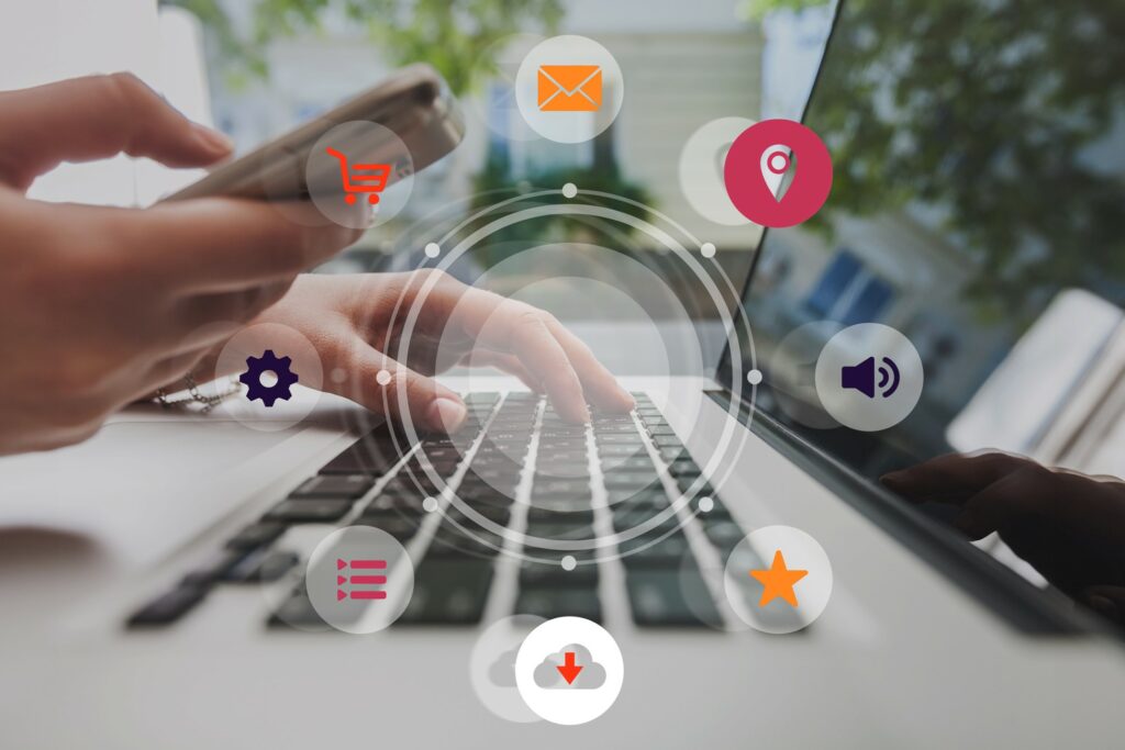 Omnichannel digital marketing concept showing hands using smartphone and laptop with icons for shopping, email, location, settings, media, downloads, and customer engagement