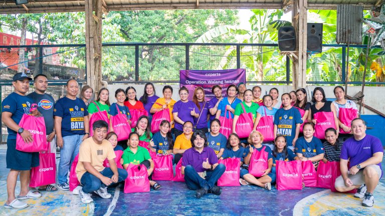 A group photo of Cxperts employees and community members during the 'Operation Walang Iwanan' CSR event. The team is seen holding pink donation bags, smiling in a sports court, underlining Cxperts' commitment to community support and customer experience. A banner in the background highlights the event's theme of partnership and giving back